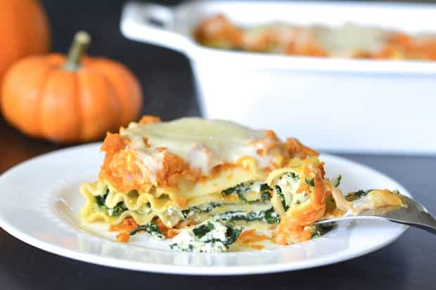 a closeup of a plate of lasgna with mini pumpkins and a family serving of lasagna in the background
