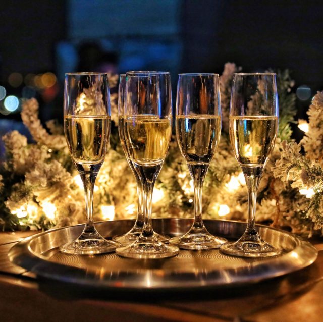 a closeup view of 4 champagne glasses with lights and a green garland behind them